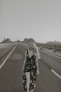 a black and white photo of a woman walking down the road in a floral dress