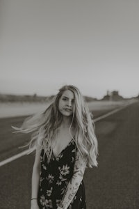 a black and white photo of a woman in a floral dress standing on a road