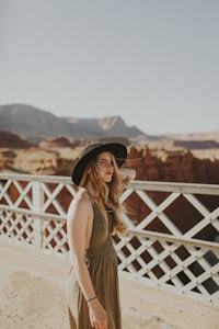 a woman wearing a hat and green dress standing on a bridge in the desert