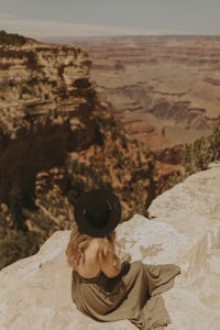 a woman sitting on the edge of a cliff overlooking the grand canyon