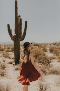 a woman wearing a red dress in the desert near a cactus