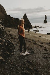 a woman standing on a black sand beach in iceland