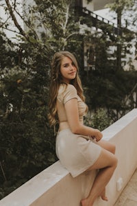 a young woman sitting on a wall in a beige skirt